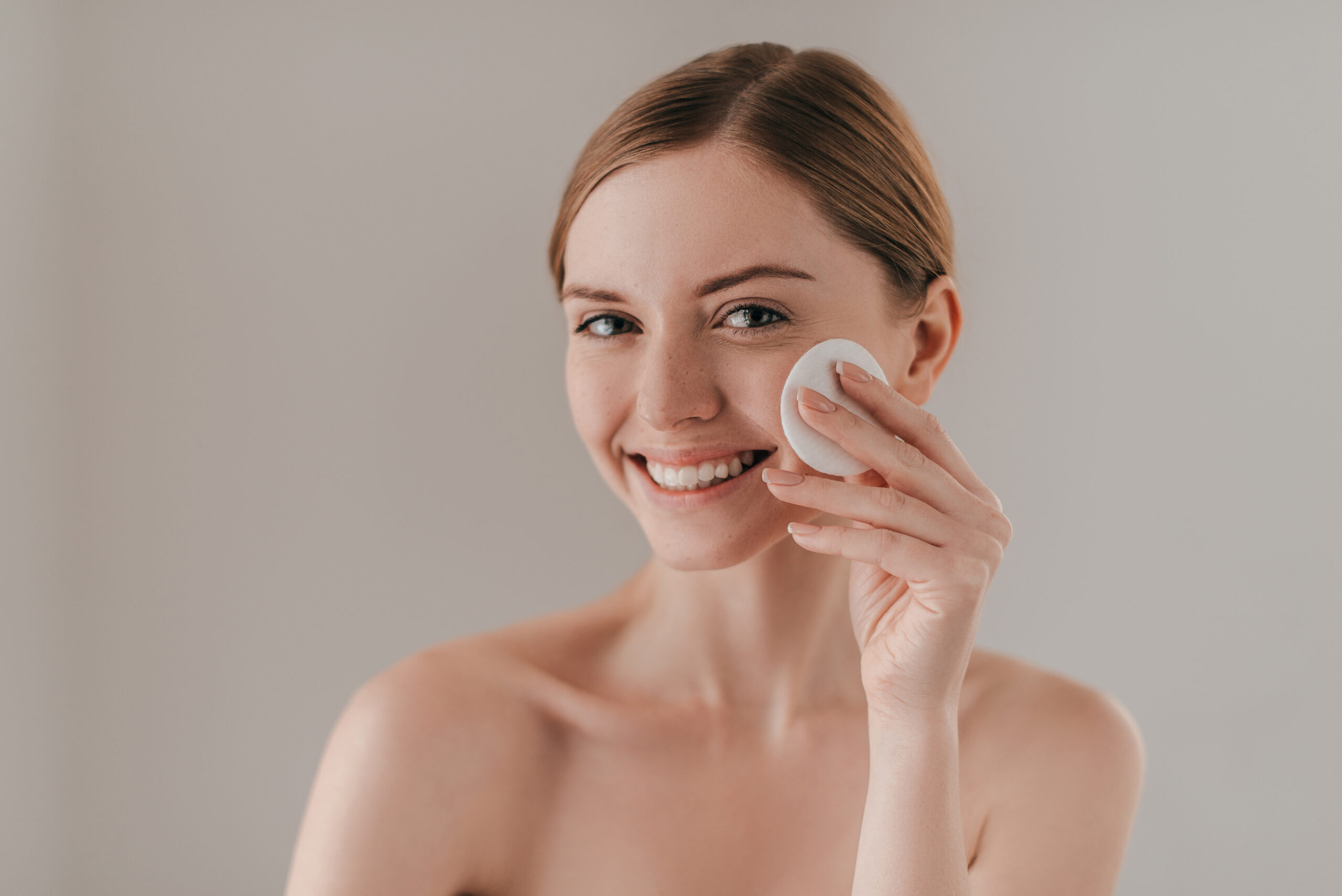 Time for skin care. Studio portrait of attractive woman cleansing her skin with a cotton pad while standing against background